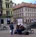 III./g Bezdomovci si rozdělují zbytky cigaret před skupinkami turistů